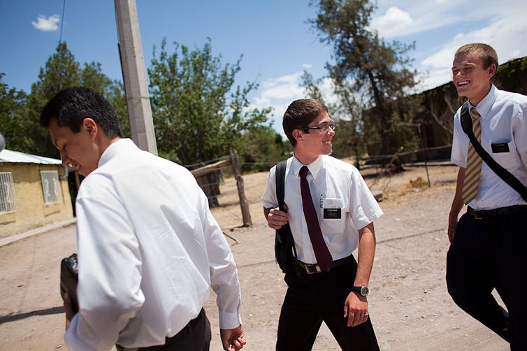 Three teen boys in white shirts and ties walk and laugh on concrete.