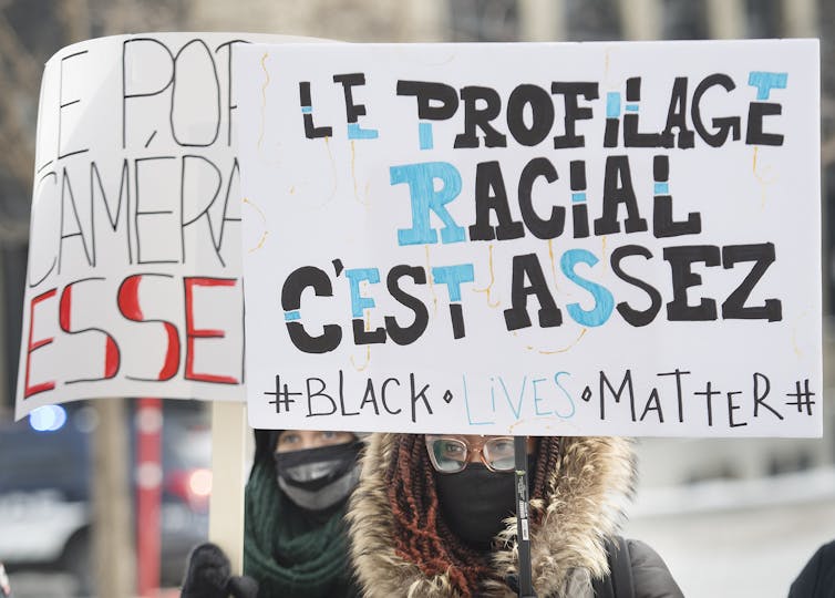 A protester in a parka holds up a sign decrying racial profiling by police.