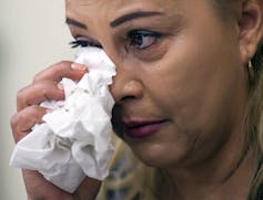 A woman weeps into a handful of tissues.