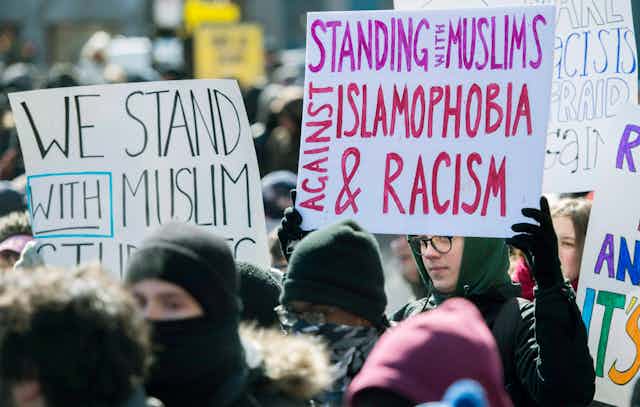 A person in a hoodie holds a sign that reads standing with muslims against islamophobia and racism