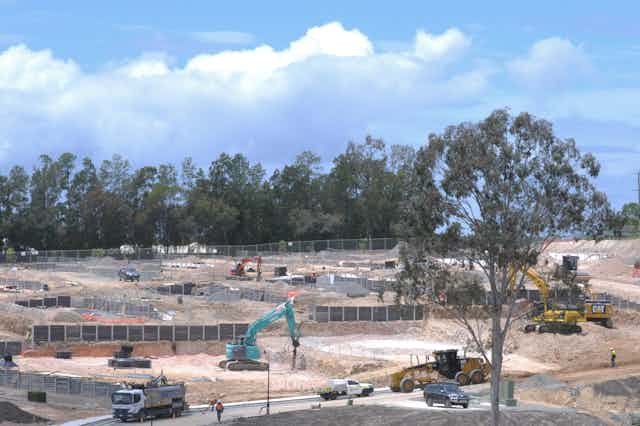 Heaving machinery and trucks on a newly cleared development site with remnant forest in the background