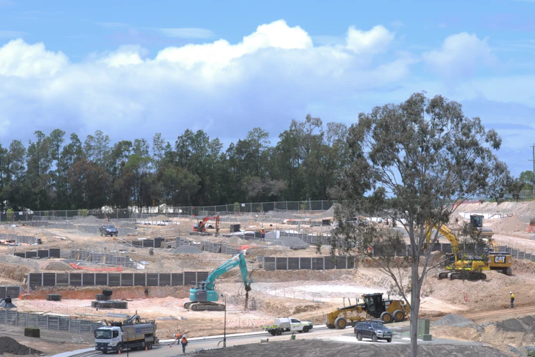 Heaving machinery and trucks on a newly cleared development site with remnant forest in the background