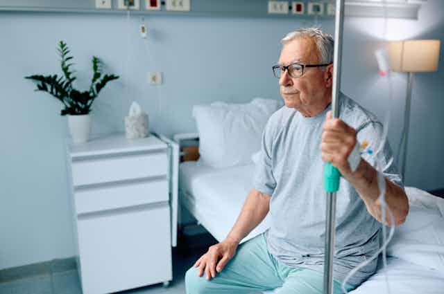 A senior man sitting on a hospital bed.