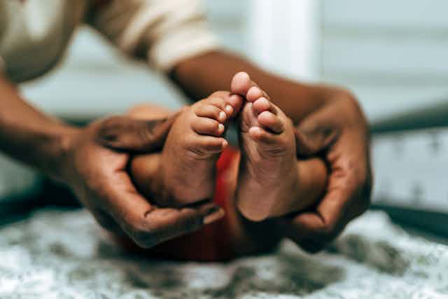 A pair of hands wrapped around a baby's feet at the ankle.