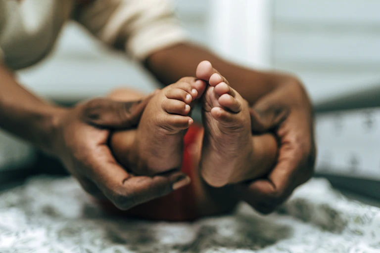 A pair of hands wrapped around a baby's feet at the ankle.
