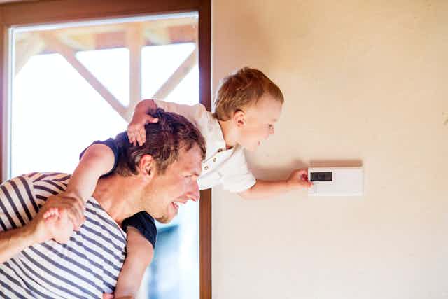 Un niño a hombros de un hombre pulsa el botón del termostato.