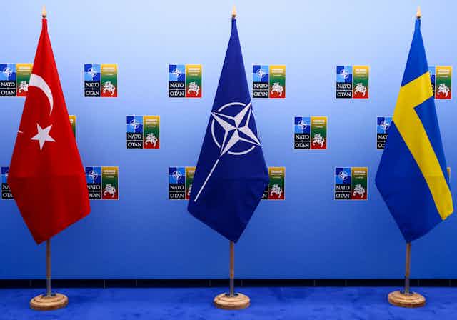 The NATO flag -- blue with a star in the center -- is flanked by the crescxent flag of Turkey and the yellow and blue cross flag of Sweden.