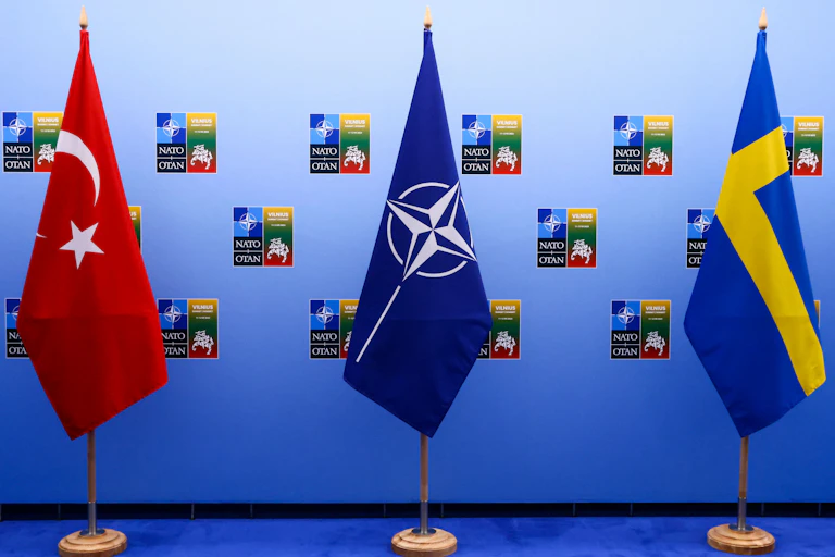 The NATO flag -- blue with a star in the center -- is flanked by the crescxent flag of Turkey and the yellow and blue cross flag of Sweden.