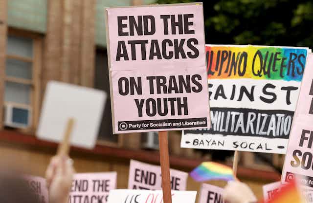 A poster on a pole that says 'END THE ATTACKS ON TRANS YOUTH'