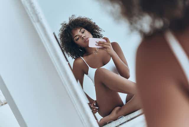 A young, clothed woman takes a sensual selfie looking into a mirror