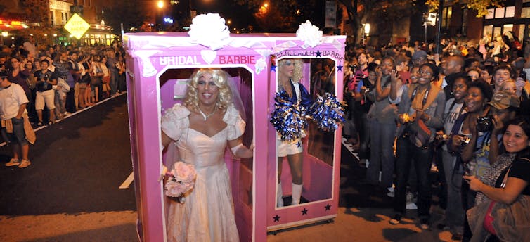 ‘Barbie Novia’ y ‘Barbie Animadora’ desfilan en un desfile antes de un evento drag en Washington, D.C., en 2010. Mark Gail / The Washington Post via Getty Images Dos drag queens desfilan por una calle vestidas con cajas rosas de Barbie para crear el efecto de ser muñecas ante multitudes de curiosos.