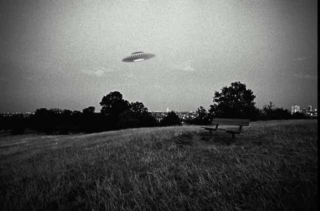 A black and white photo showing a flying saucer over an empty field.