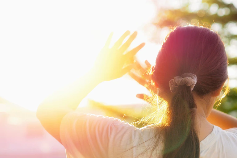 Une jeune fille se protège du Soleil, mains levées