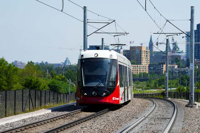 A light rail train travels along tracks while a city skyline is seen in the distance