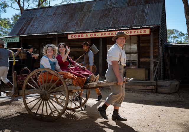 Production image: two women in a cart drawn by a man.