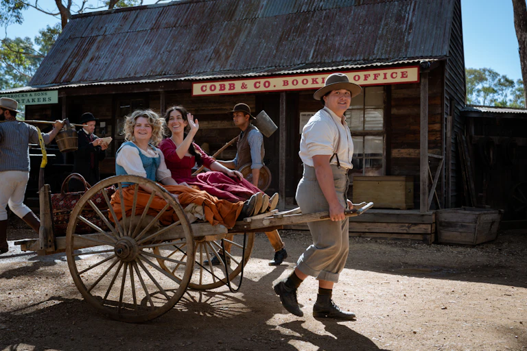 Production image: two women in a cart drawn by a man.