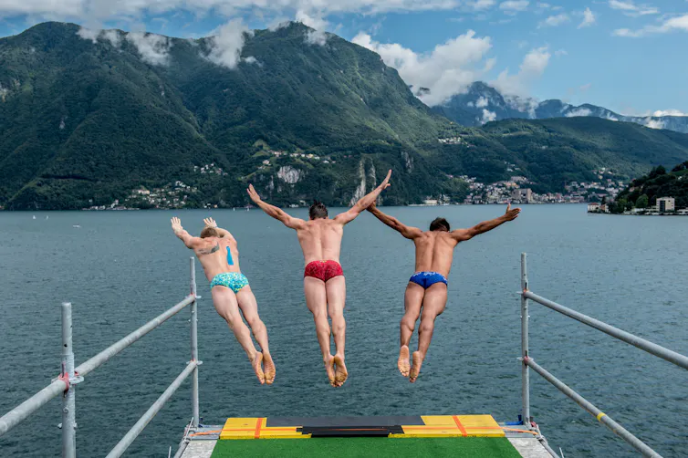 three people dive into a lake