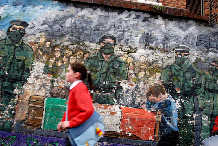 A child in school uniform walks past a mural.