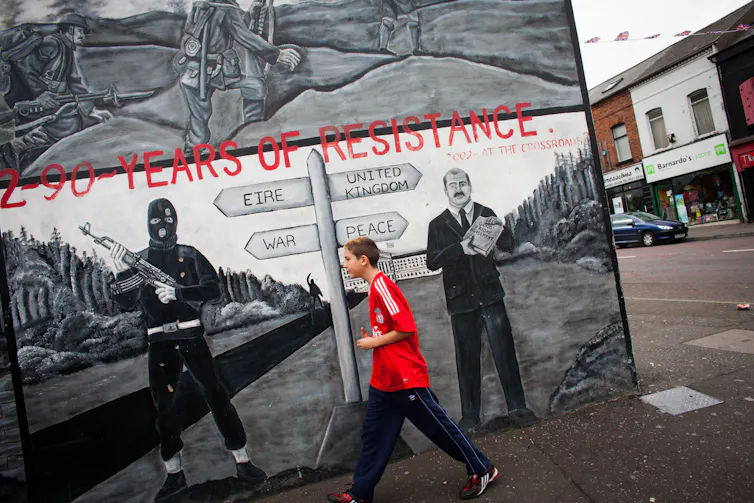 A boy in a red shirt walks past a mural.