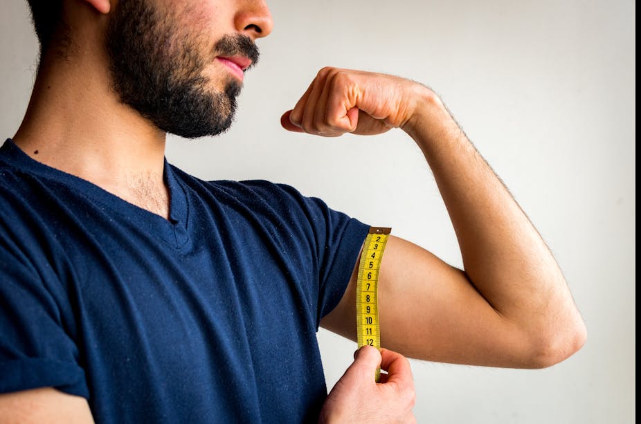 A man flexing his bicep while measuring it with a measuring tape.