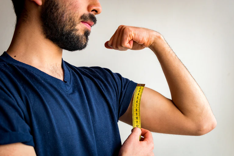 A man flexing his bicep while measuring it with a measuring tape.