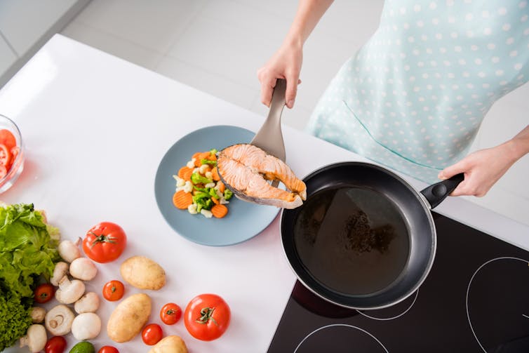 A person scoops cooked salmon from a pan and onto a plate.