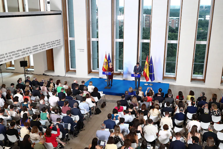 A woman and a man stand in front of dozens of journalists seated and waiting for them to talk.