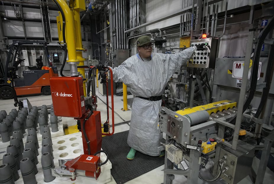 A man in a gray protective gear in a space full of pipes and equipment.
