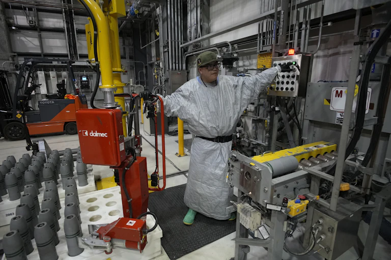 A man in a gray protective gear in a space full of pipes and equipment.