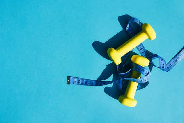 Yellow dumbbells with blue tape measure wrapped around them