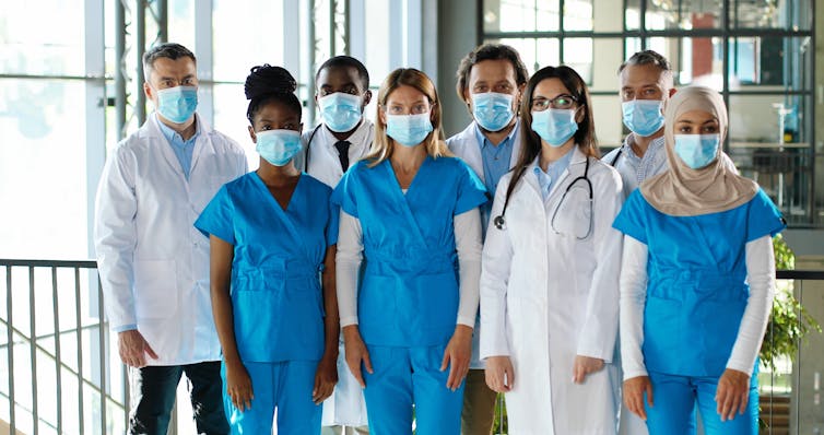 Health workers in scrubs and white coats wearing face masks