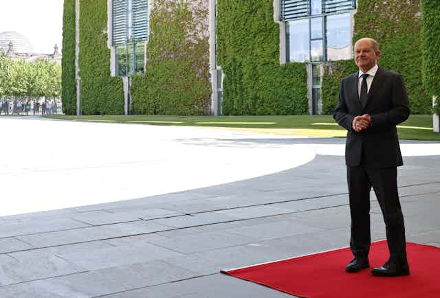 Olaf Scholz standing alone on a red carpet.