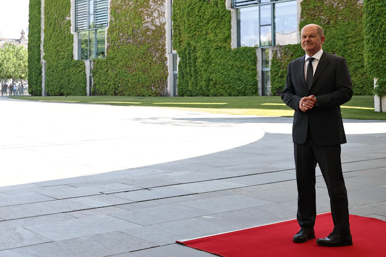 Olaf Scholz standing alone on a red carpet.