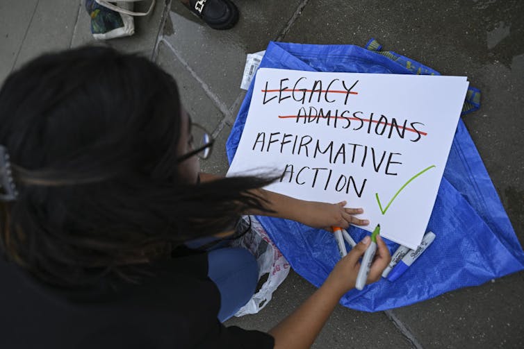 a person hunches over a poster showing support for affirmative action but not legacy admissions.