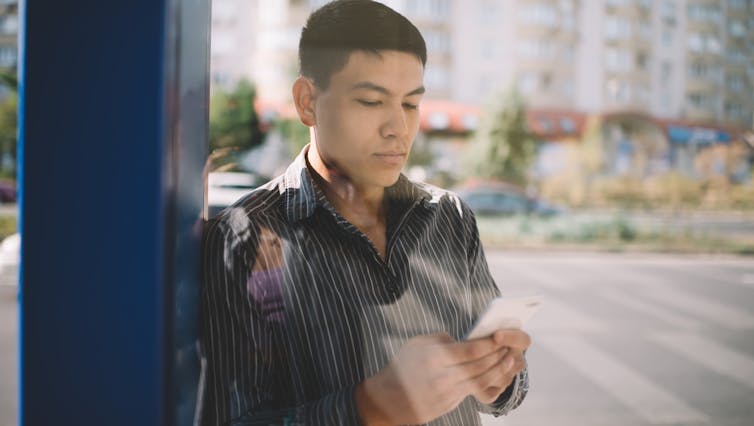 a young man in a leather jacket looks at his phone while waiting at the bus