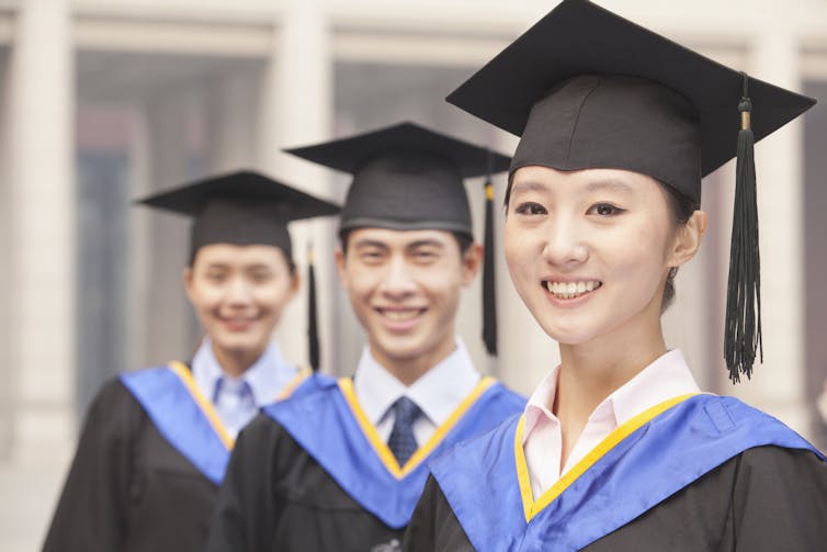 Three students wearing mortarboards and graduation gowns.