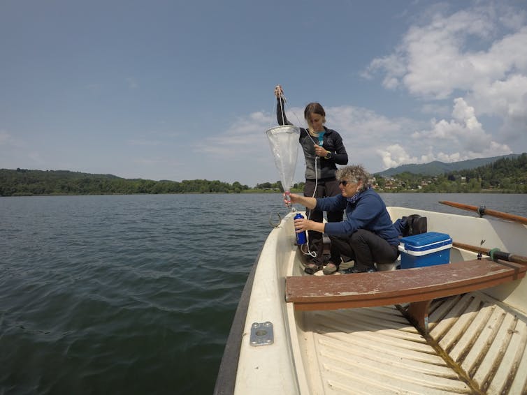 Two women take samples from a boat on a lake.