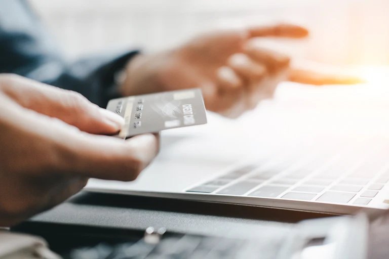 hand holding credit card near open laptop computer