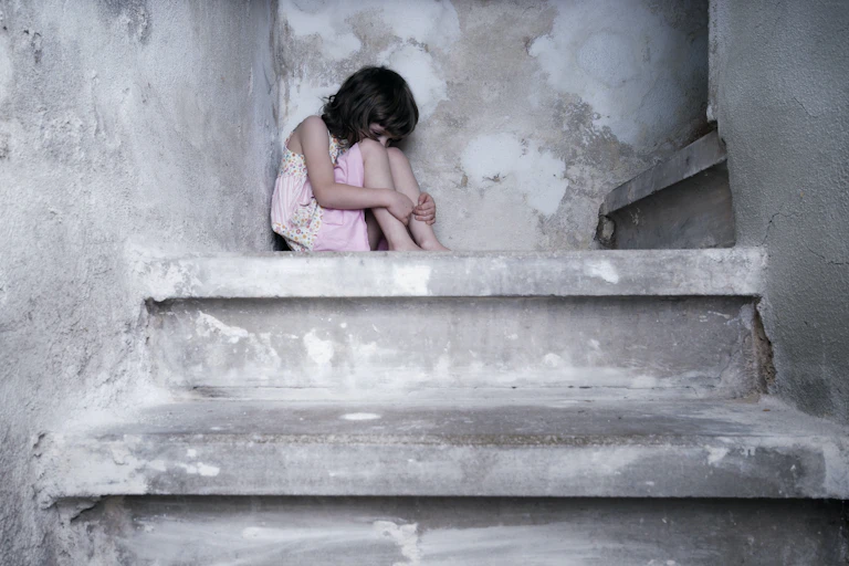 Niña acurrucada en una escalera.