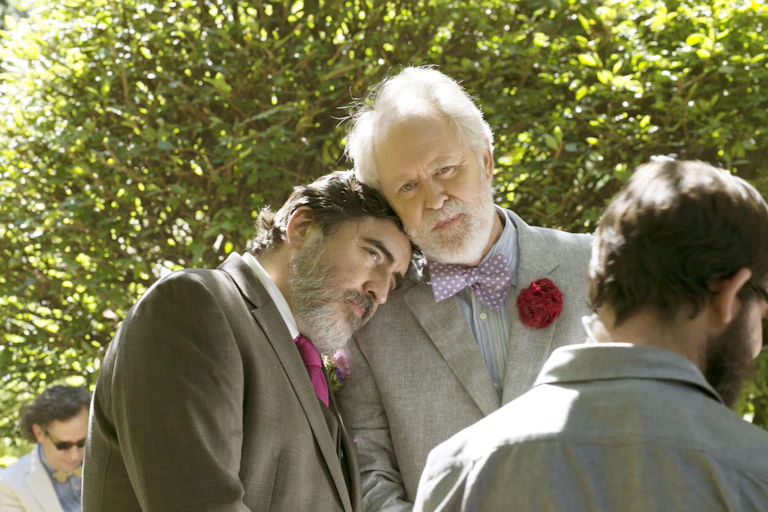 Alfred Molina and John Lithgow resting heads on each other while wearing suits.