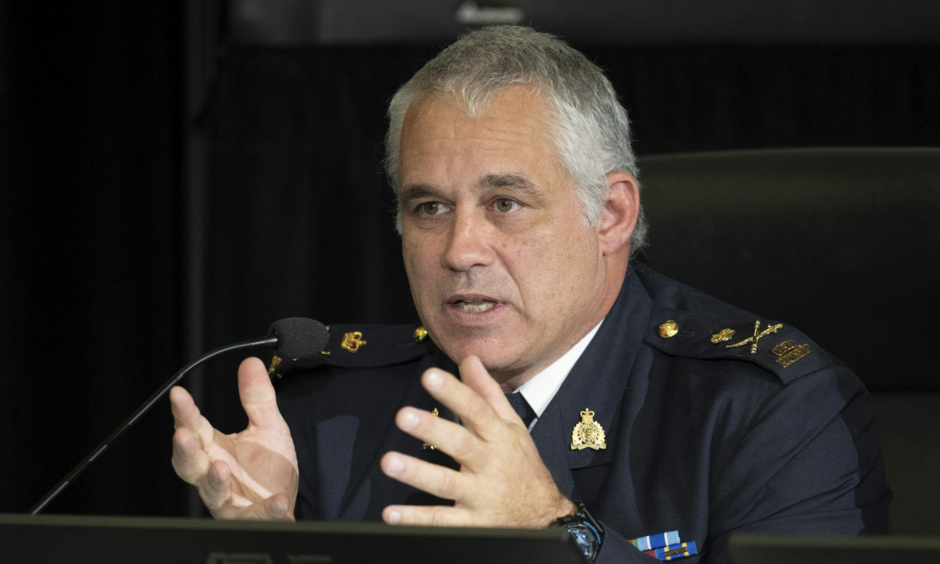 A grey-haired man in uniform gestures as he speaks.