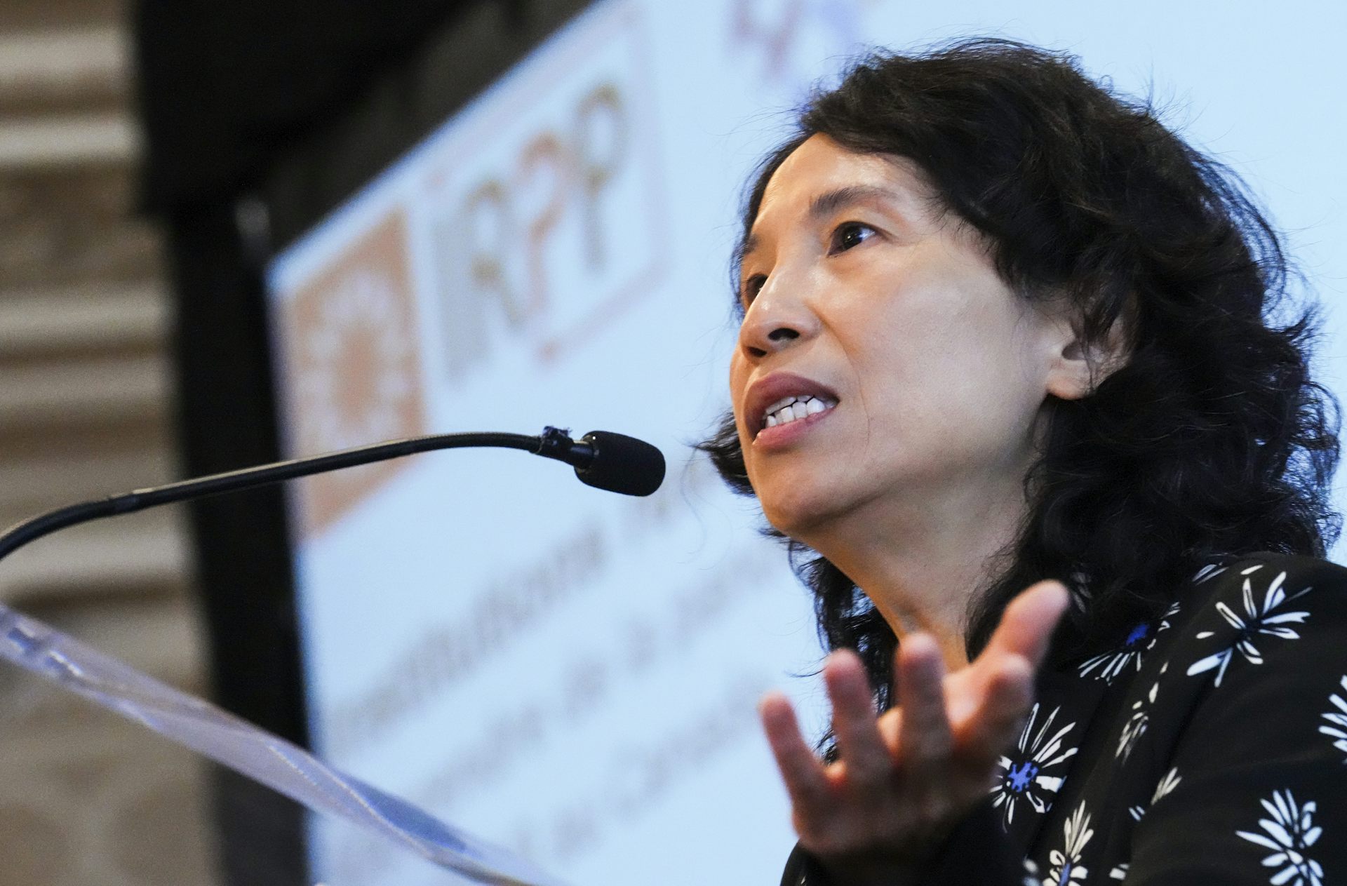A dark-haired woman speaks into a microphone.