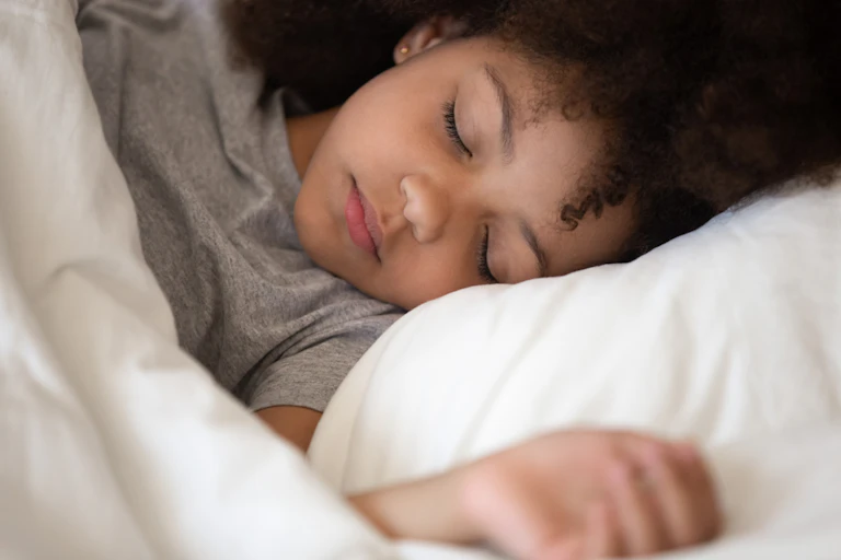 Petite fille qui dort dans son lit avec un oreiller blanc et une couette