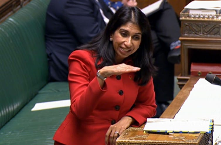 Suella Braverman in a red suit, speaking at the podium in the House of Commons
