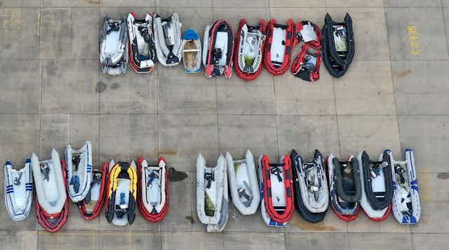 Overhead view of about two dozen empty, inflatable boats arranged in two rows on a concrete lot