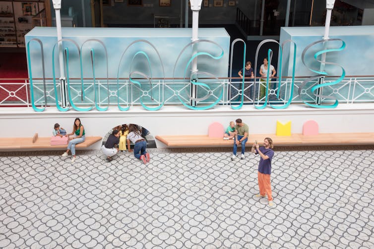 Wire spelling the word 'IMAGINE' with kids playing underneath.