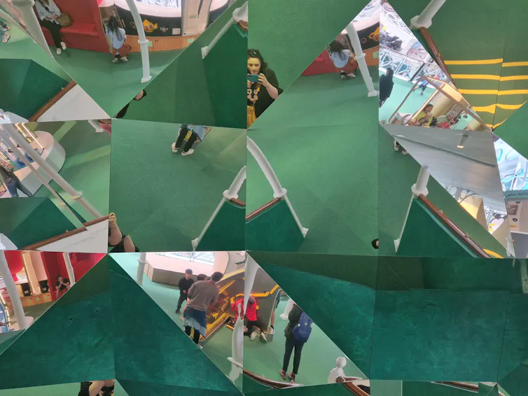 multifaceted glass reflective ceiling, showing reflection of a green carpet and people looking upwards.