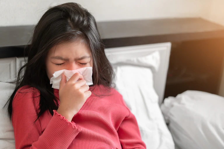 A sick child blows her nose into a tissue.