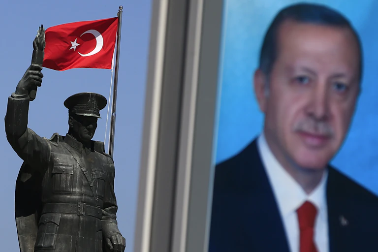 A portrait photo of Recep Tayyip Erdogan is seen next to a flag of Turkey and a bronze statue of a soldier or man wearing a hat.