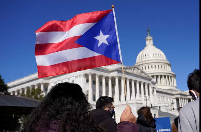 A woman waves a Puerto Rican flag. The Capitol building is visible in the background.